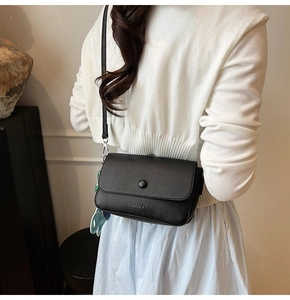 Detail of black lychee grain crossbody bag with flap cover and elephant charm accessory