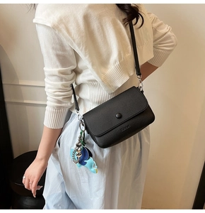 Detailed texture of black litchi grain leather shoulder bag with an elephant charm