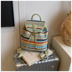 Détail d'un sac à dos tissé à rayures colorées avec rabat en cuir vert sur une valise