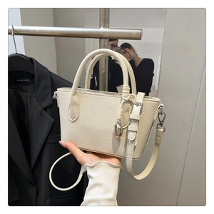 Gros plan d'un sac à main beige en cuir grainé avec pendentif coeur et bandoulière