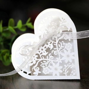 Close-up of white heart-shaped wedding favor box with laser-cut floral details and ribbon