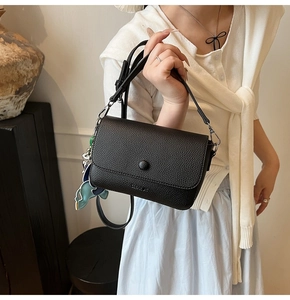 Detail of black lychee grain crossbody bag with round buckle and cartoon pendant charm