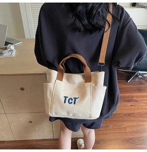 Détail du sac fourre-tout en toile blanche avec bandoulières brunes et broderie TCT
