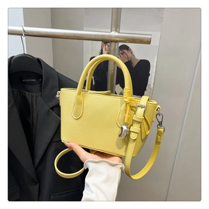 Détail d'un sac seau jaune en cuir grainé avec un pendentif décoratif en métal argenté