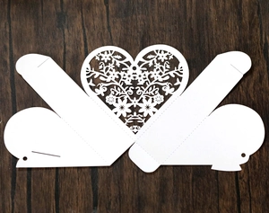 Flat lay of white laser-cut wedding favor box showing detailed hollow heart pattern