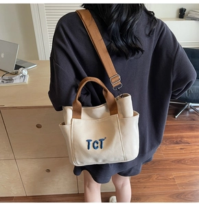 Détail du cabas en toile avec poignées marron et broderie TCT porté par un mannequin