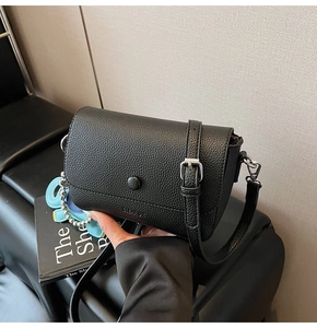 Detail of black lychee grain leather square bag with snap closure and cartoon charm