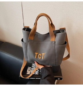 Détail du sac fourre-tout en toile grise avec anses brunes et broderie TCT jaune