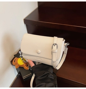 Detail of cream white lychee leather square bag with cute orange elephant charm and strap