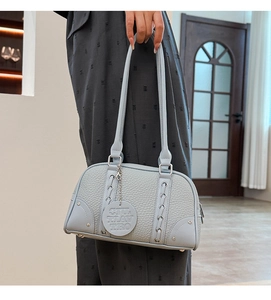 Detail of light blue pebble leather texture with rivets and round logo tag on handbag