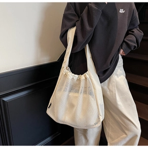 Detail of a large cream mesh tote bag with canvas straps on a female model