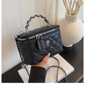 Détail du sac seau matelassé en cuir noir avec poignée en chaîne et décoration logo camélia