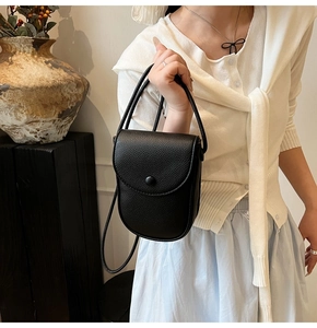 Petit sac bandoulière noir en cuir grainé porté par un mannequin dans un décor épuré