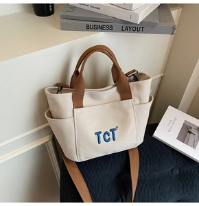Détail du sac cabas en toile avec sangles brunes, poches latérales et logo brodé bleu
