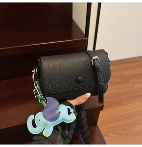 Close-up of black lychee grain leather crossbody bag with a blue elephant charm