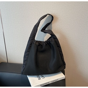 Detail of black mesh tote bag showing large aperture hollow nylon texture on a casual prop