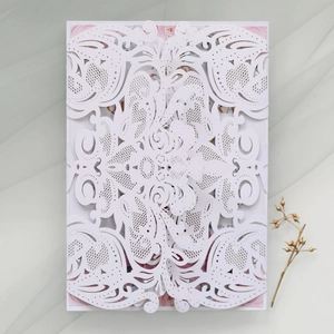 Detail of laser-cut white wedding invitation sleeve with floral insert on fabric