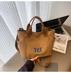 Détail d'un sac cabas en toile kaki montrant plusieurs poches et broderie TCT bleue