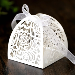 Macro shot of laser-cut rose patterns on white wedding favor box with organza ribbon