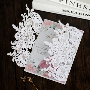 Close-up of laser-cut wedding invitation with floral insert on dark wood surface