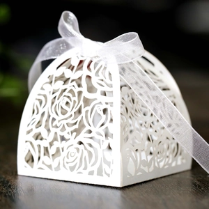 Detailed laser-cut white rose favor box with elegant satin ribbon bow on dark wood background