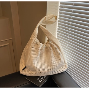 Detail of beige mesh tote bag with wide shoulder straps and drawstring closure on a leather base