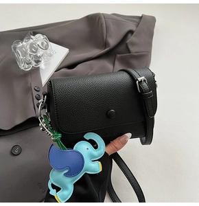Detail of black lychee grain leather crossbody bag with cute elephant charm accessory