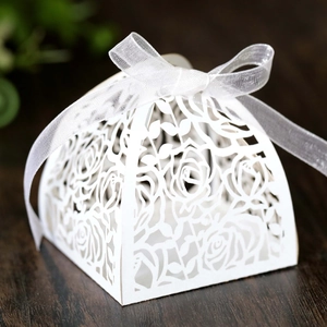 Detail view of laser-cut rose hollow candy box with white silk ribbon on wooden desk
