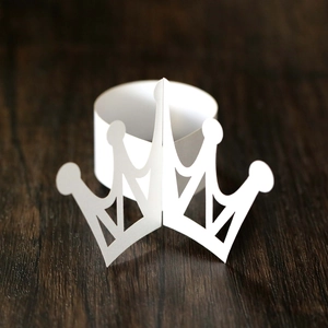 Close-up of white paper crown napkin ring with intricate laser-cut patterns for parties
