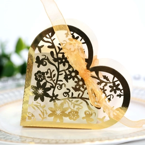 Golden laser-cut heart wedding favor box with ribbon on a decorative ceramic plate