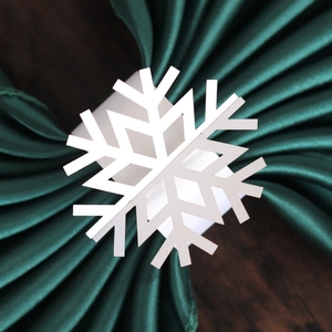 Detailed close-up of a white laser-cut snowflake napkin ring on green satin and wood