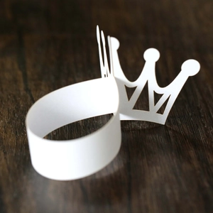 Close-up of white paper crown napkin ring with laser-cut edges on a wooden surface