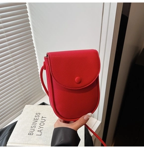 Détail du mini sac à bandoulière rouge texture litchi avec fermeture à rabat à la main