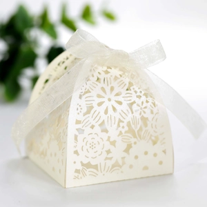 Detail of laser-cut cream wedding favor box with intricate floral patterns and white ribbon bow