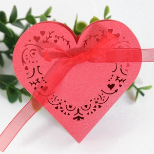Detail of red heart-shaped laser-cut wedding favor box with ribbon and vine patterns
