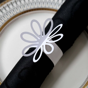 Macro view of white paper flower napkin ring with hollow petals on a black napkin