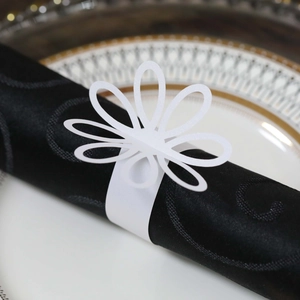 Detail of white laser-cut floral napkin ring on black cloth with elegant dinnerware