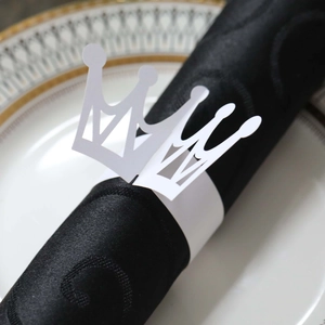 Close-up of white paper crown napkin ring with laser-cut design on black napkin