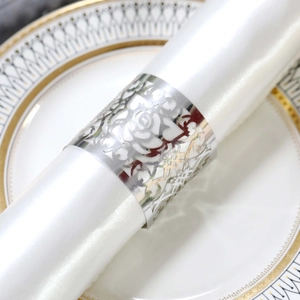 Close-up of silver hollow floral napkin ring on a white satin cloth with a plate