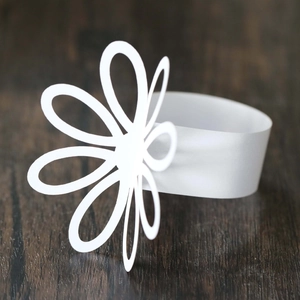 Detail of white laser-cut floral paper napkin ring on dark wood surface