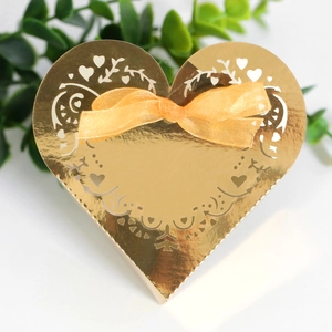 Close-up of laser-cut heart pattern on gold wedding candy box with orange silk ribbon