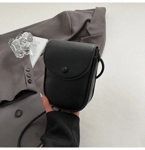 Détail d'un sac bandoulière en cuir noir grainé avec fermeture à bouton et bandoulière