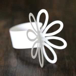Detailed view of a white cutout flower napkin ring on a dark wooden textured surface