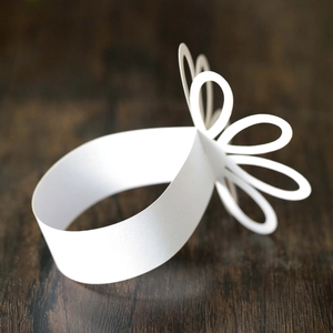 Close-up of a white paper napkin ring with 3D floral design on a wooden table