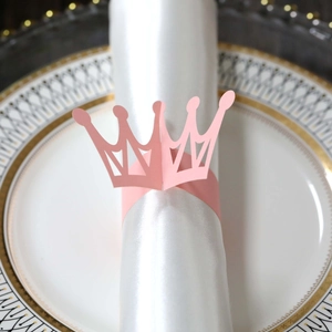 Detail of pink crown paper napkin ring on a white napkin over a fine gold-rimmed china plate