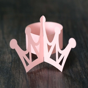 Close-up of pink hollow-out crown paper napkin ring on a dark wood background