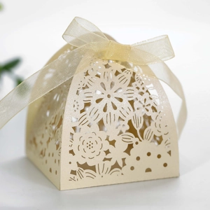Detail of laser-cut beige favor box with hollow floral patterns and gold silk ribbon