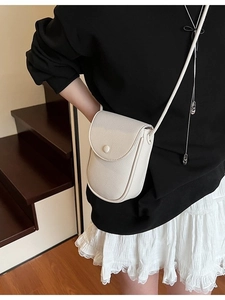 Petit sac bandoulière pour femme en cuir crème avec boucle ronde sur un escalier