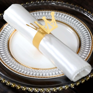 Close-up of golden crown napkin ring with matte glitter finish on a white satin napkin