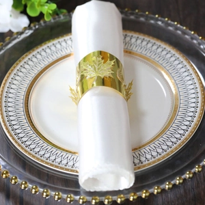 Dettaglio portatovagliolo foglia d'acero dorata su tessuto bianco per decoro tavola
